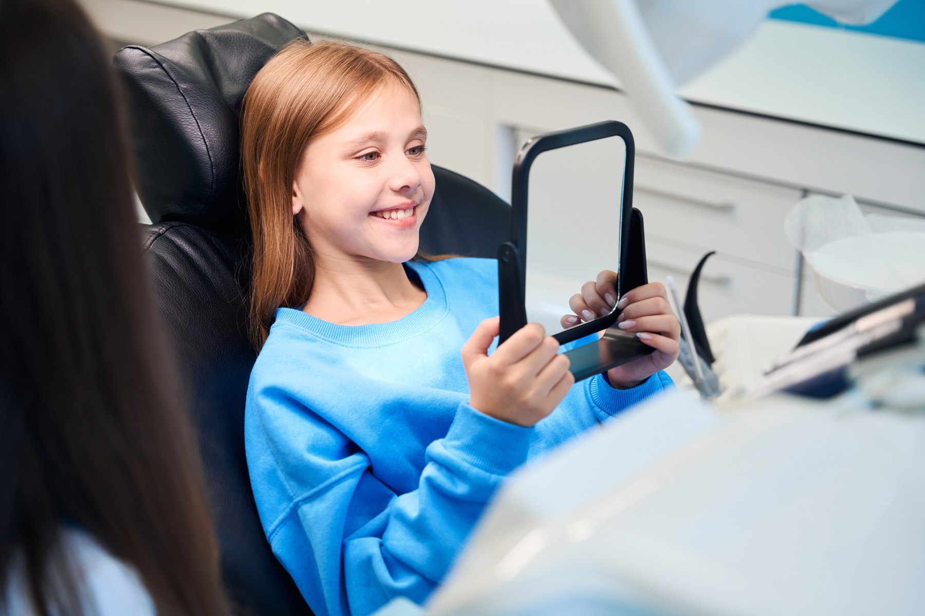 Child smiling while holding a dental mirror